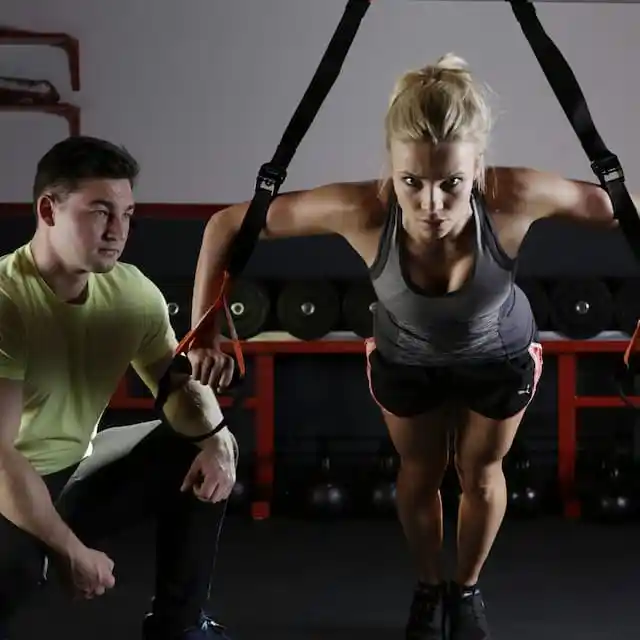 A trainer spots a woman's technique on functional equipment